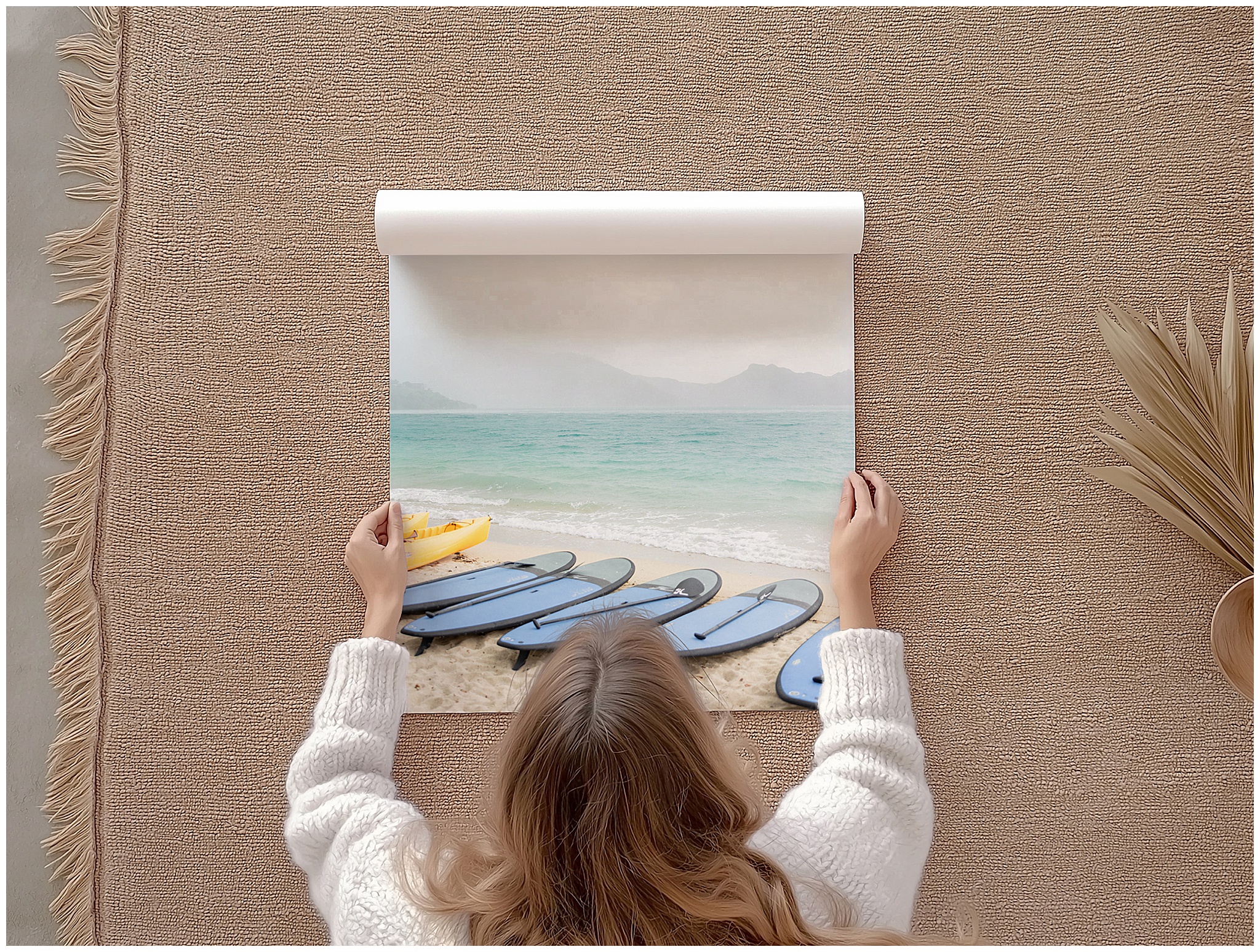 Overhead photo of a woman gently rolling a Hayman Island landscape print with paddle boards, shown as a mockup to highlight the fine art print quality and packaging.